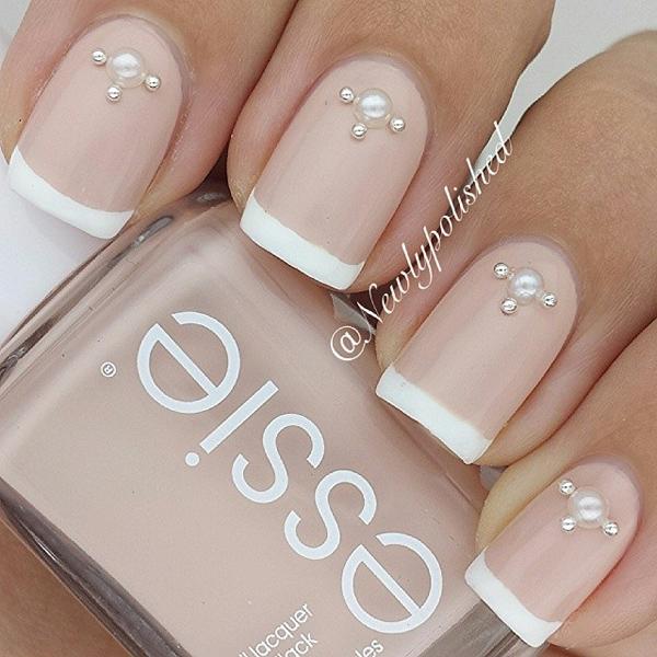 Nude and white nail polish combination. This nail art design uses nude nail polish with white French tips. Additional pearl and gold beads are also added on top for effect.