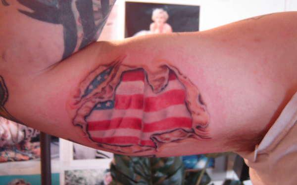 Ripped skin tattoo on bicep with American flag inside