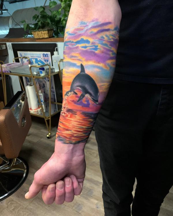Dolphin jumping out of sunset water under clouds tattoo