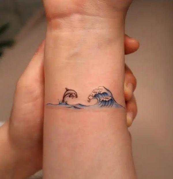 Dolphin jumping out wave inner forearm tattoo