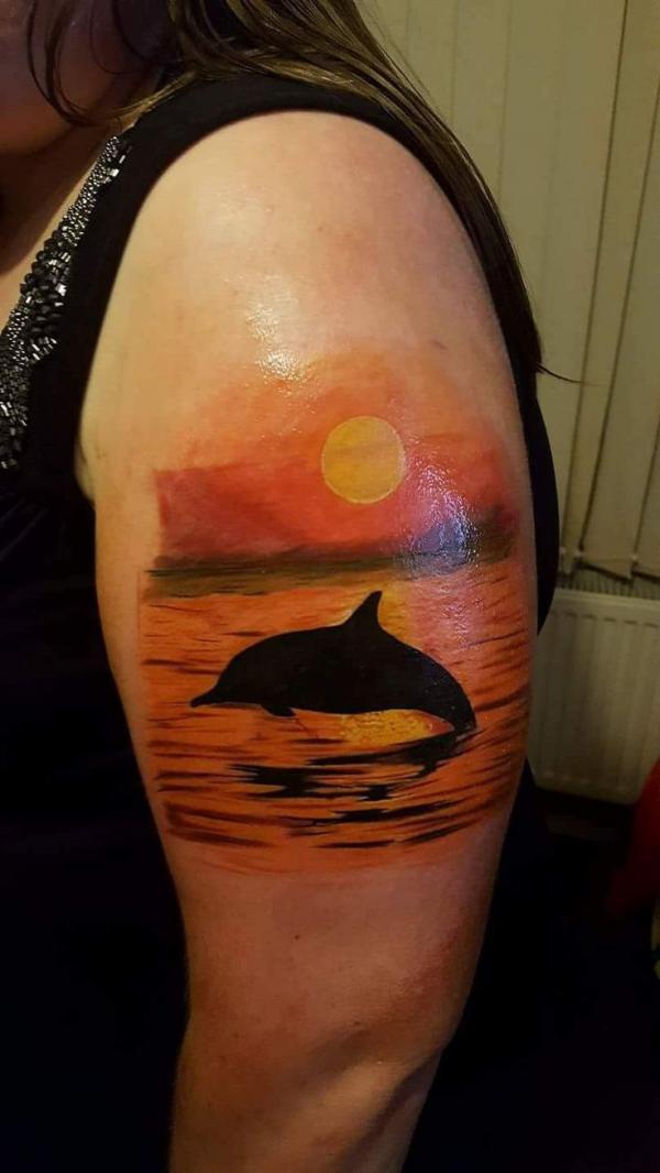 Dolphin sunset upper arm tattoo