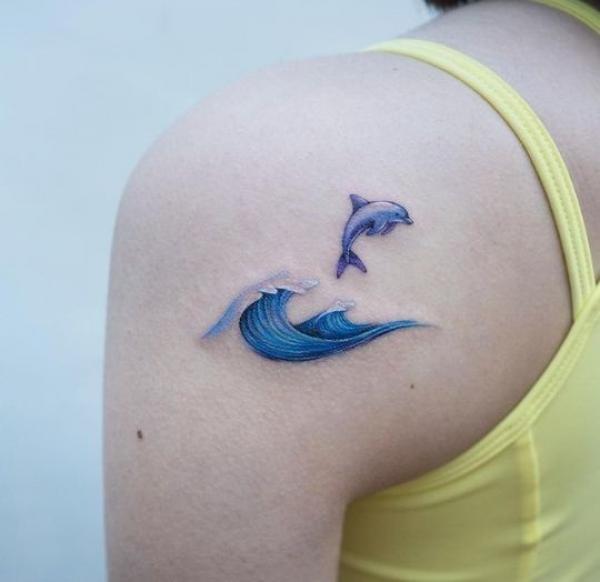 Minimalist dolphin and wave shoulder tattoo