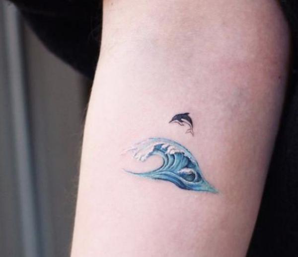 Tiny dolphin and wave arm tattoo