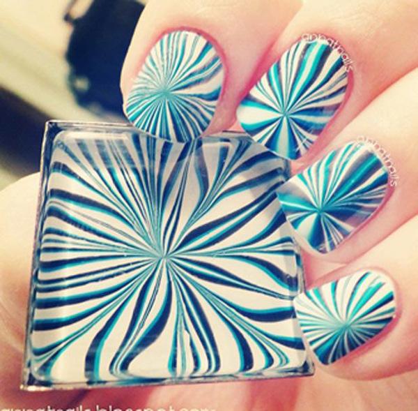 A radical and sassy water marble nail art design in white, blue and green blue polish patterned together to create intersecting lines.