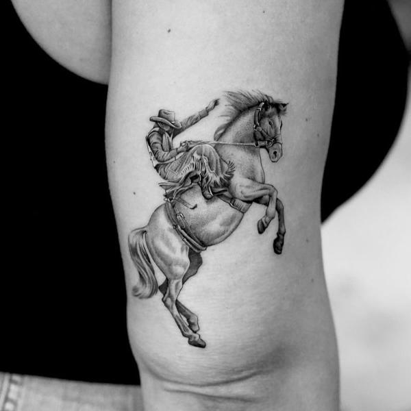Cowboy riding a horse back of arm tattoo
