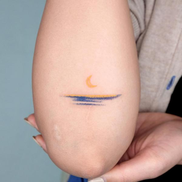 Minimalist tattoo of crescent moon on the horizon on the forearm