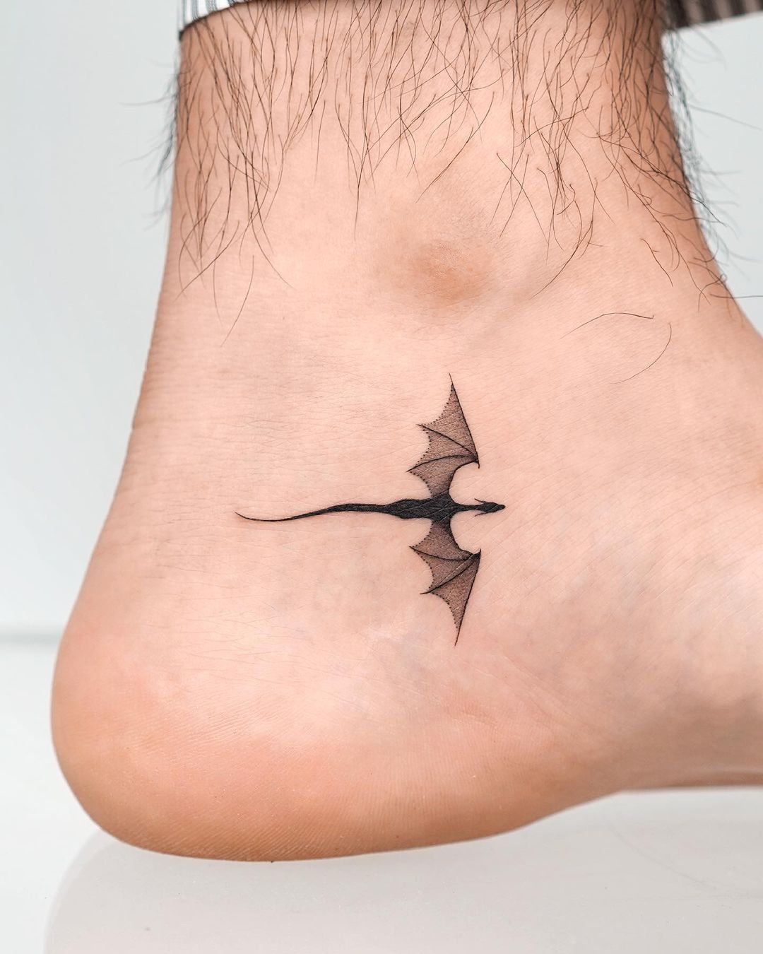 A small tattoo of a bat gliding in the air on the ankel