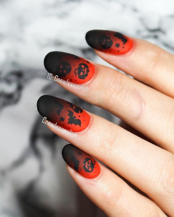 Halloween nail in oval shapes with black gradients applied to a red manicure bed and adorned with bats and other Halloween symbols. 