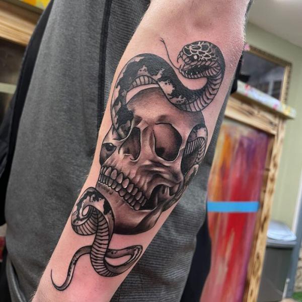 A snake through a skull forearm tattoo
