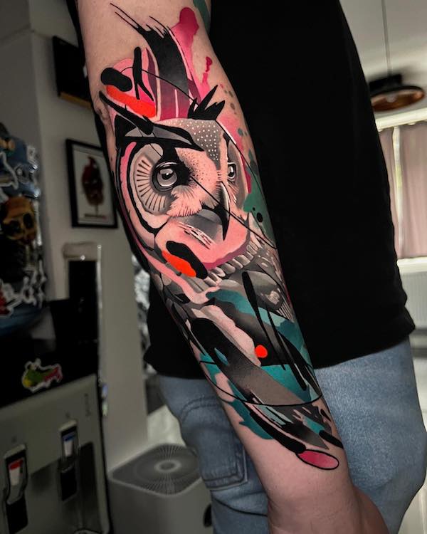 An owl forearm tattoo with vivid watercolor splatters