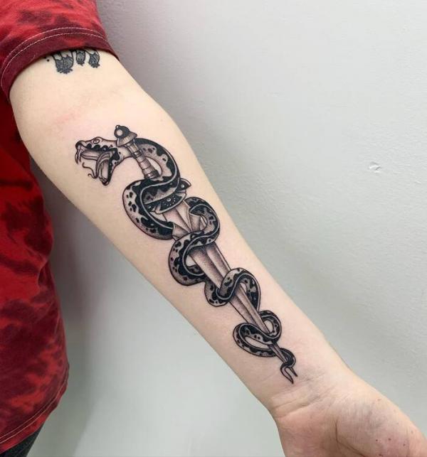 Black and white coiled snake and dagger forearm tattoo