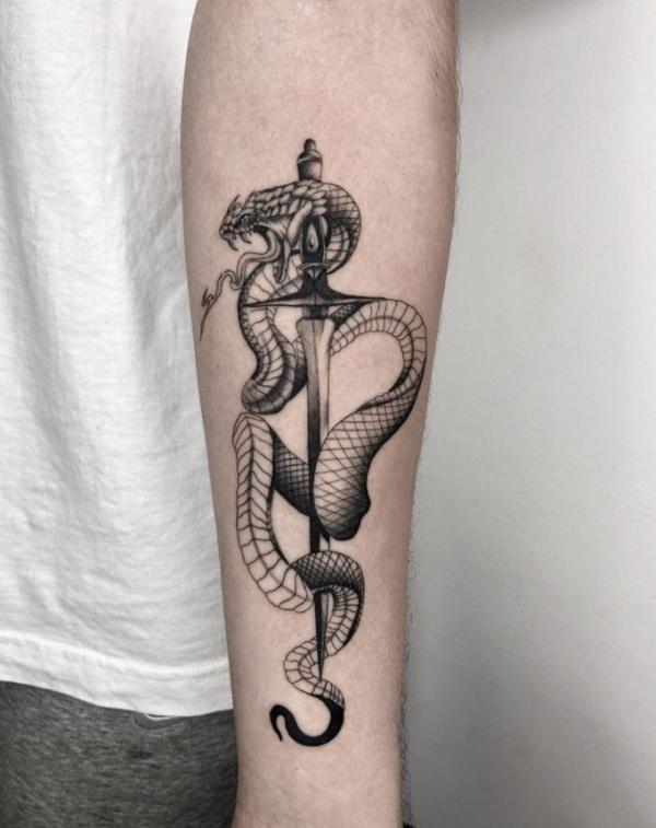 Black and white dagger snake tattoo on forearm