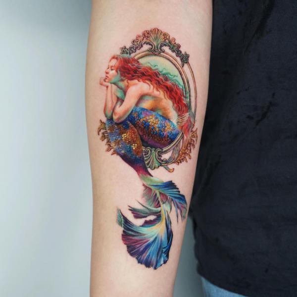 Colored mermaid sitting on a frame tattoo