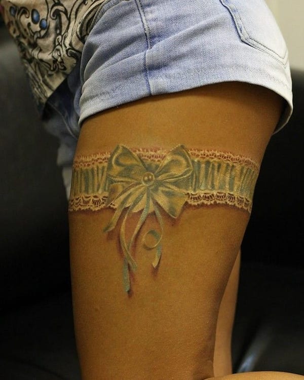 Lace and ribbon garter tattoo on thigh