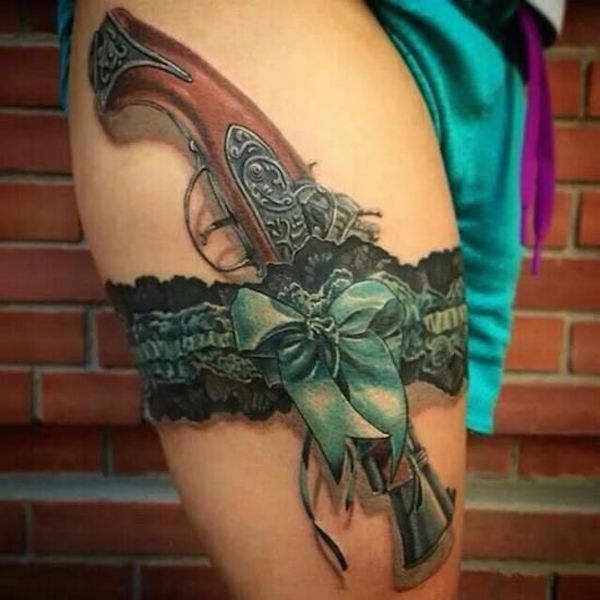 Old revolver and green ribbon bow garter tattoo