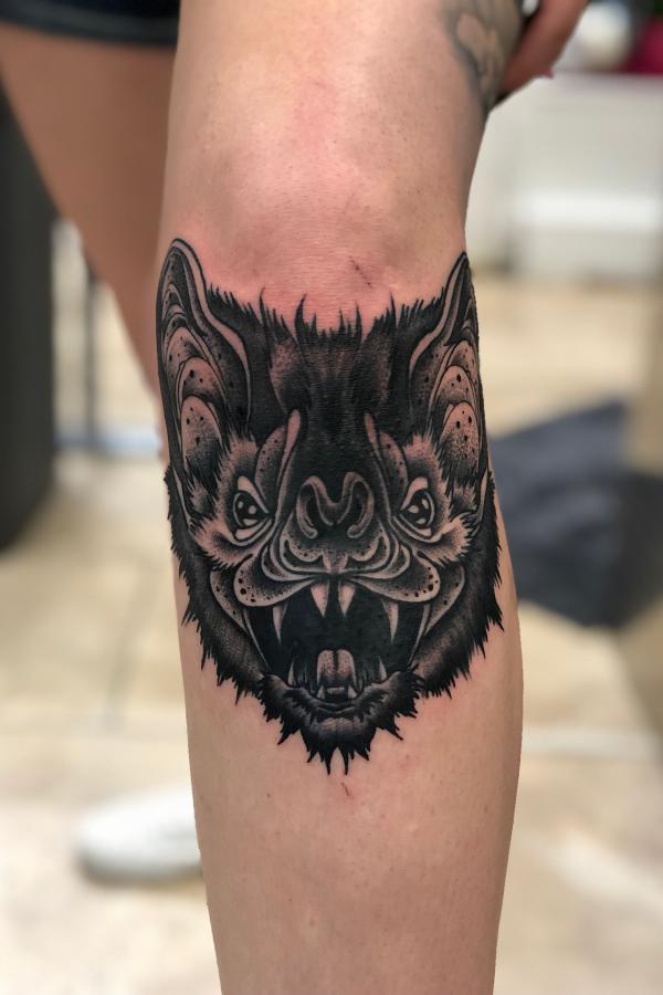 Stylized bat face knee tattoo