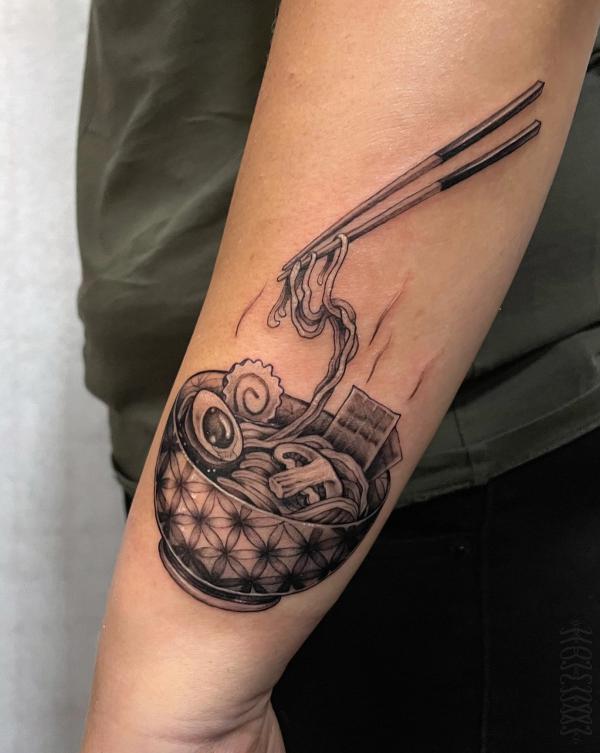 A pair of chopsticks picking up noodles from a bowl with flower of life texture on its surface