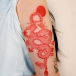Red dragon and sun tattoo on upper arm