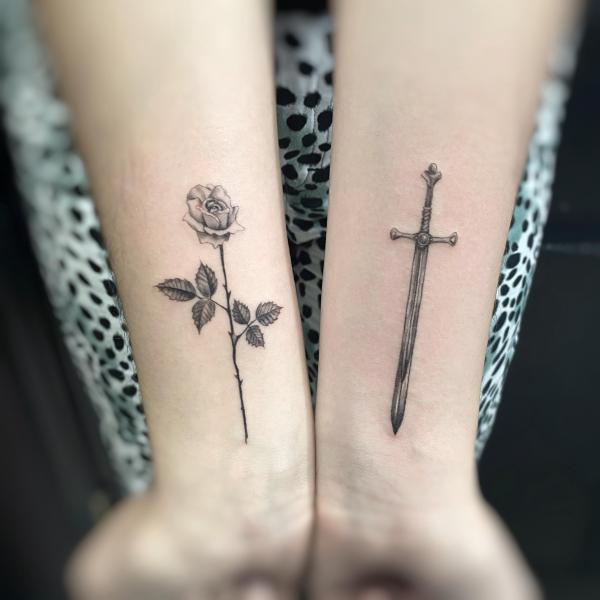 A dagger and a stem of rose tattoo black and grey