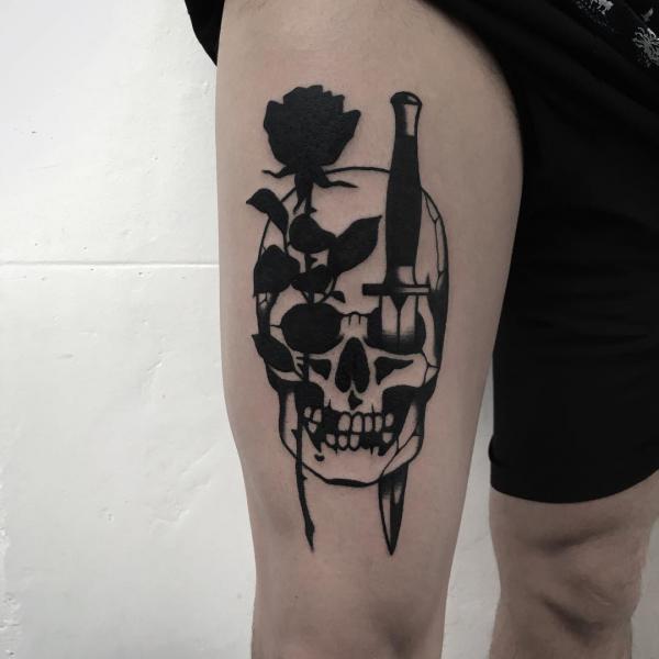 Black ink rose and dagger through a skull tattoo