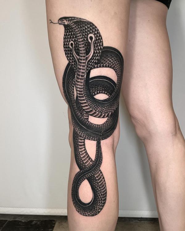 Coiled black cobra tattoo on leg