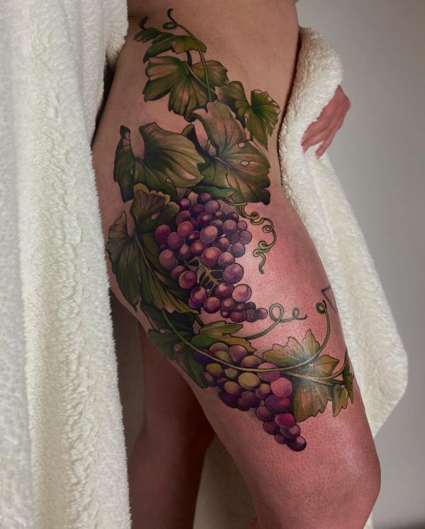 Grapes with vine and leaves tattoo on the side of hip and thigh