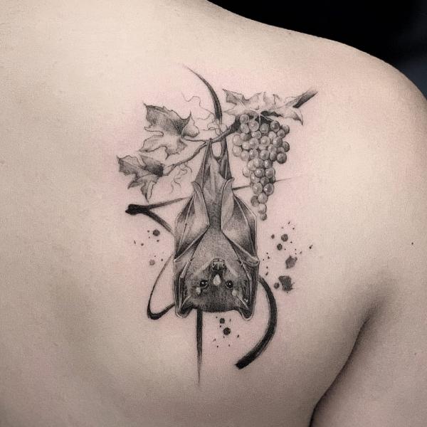 Hanging bat upside down on branch of grape shoulder blade tattoo