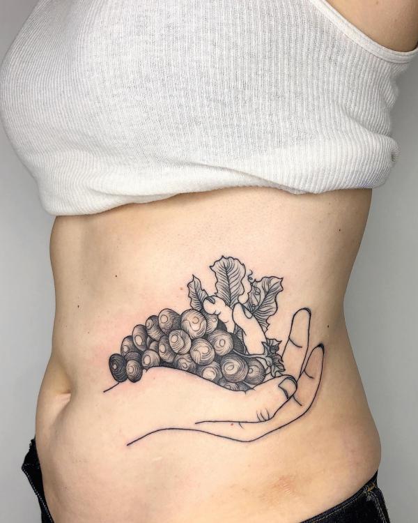 Negative space hand holding grapes side tattoo