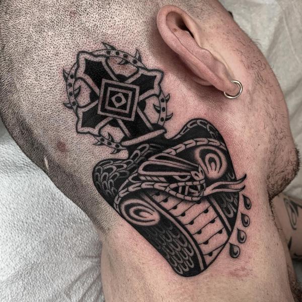 Stylized cobra head and cross tattoo behind ear