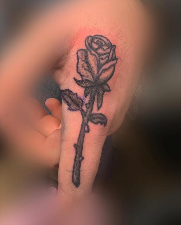 Black and grey rose tattoo on the side of index finger