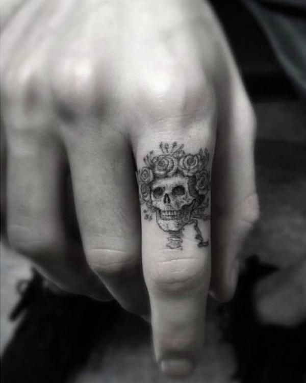 Black and grey skull with roses tattoo on index finger