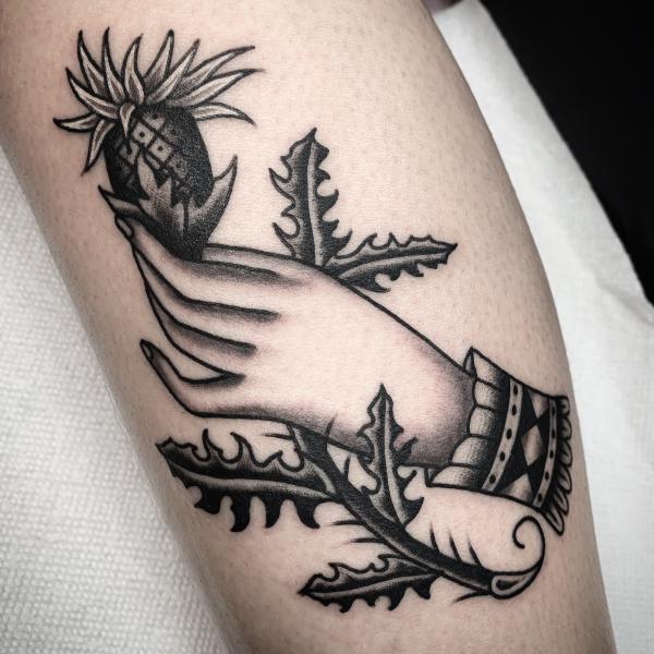 Black and white traditional hand holding thistle tattoo