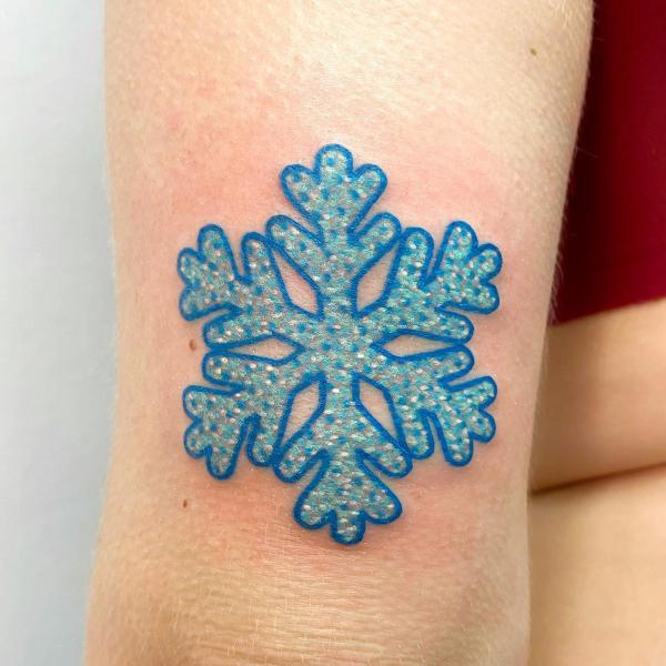 Blue snowflake tattoo above elbow