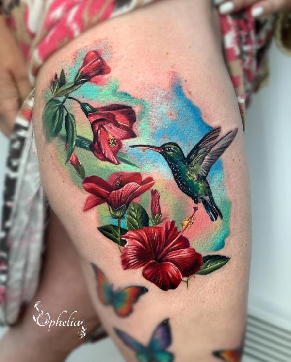 Hummingbird and hibiscus thigh tattoo on watercolor backdrop