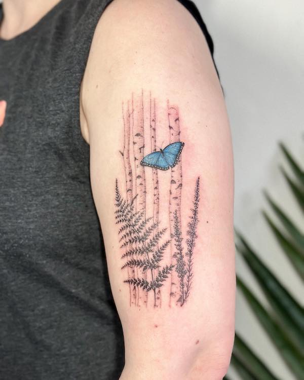 A blue butterfly flying over fern upper arm tattoo