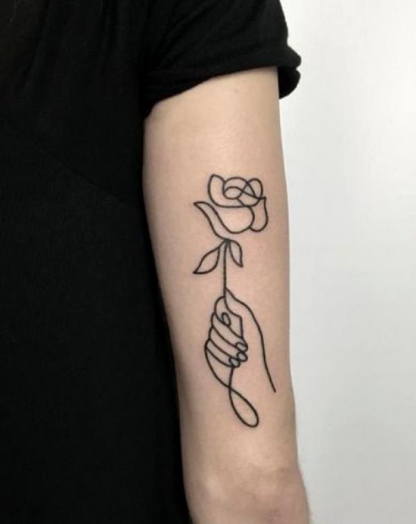 A hand holding a rose outline tattoo