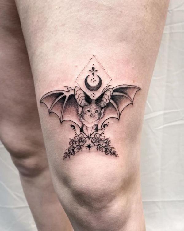 Bat and moon with flowers above knee tattoo