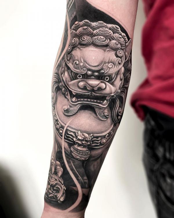 Black and grey foo dog with ball forearm tattoo