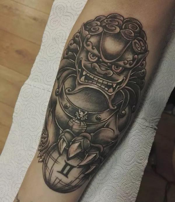 Black and grey foo dog with ball inner forearm tattoo