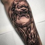 Black and grey foo dog with ball tattoo forearm