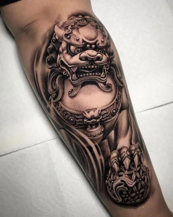 Black and grey foo dog with ball tattoo forearm