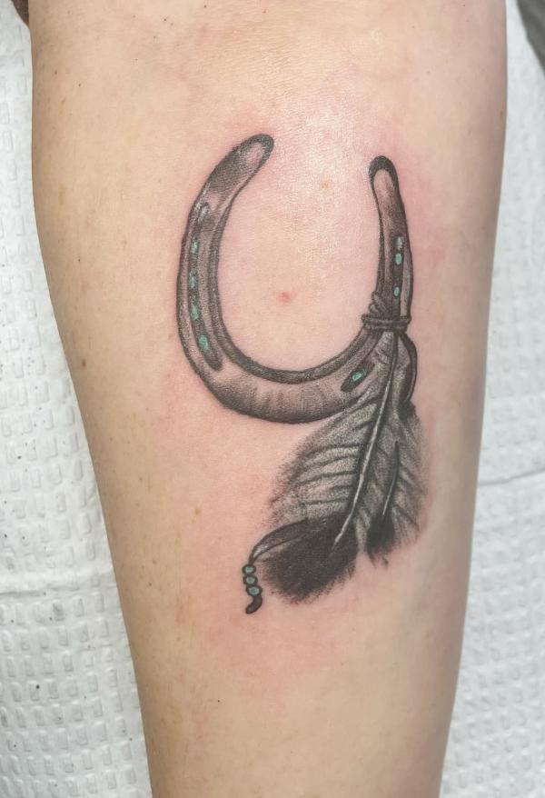 Black and grey horseshoe and feather tattoo on thigh