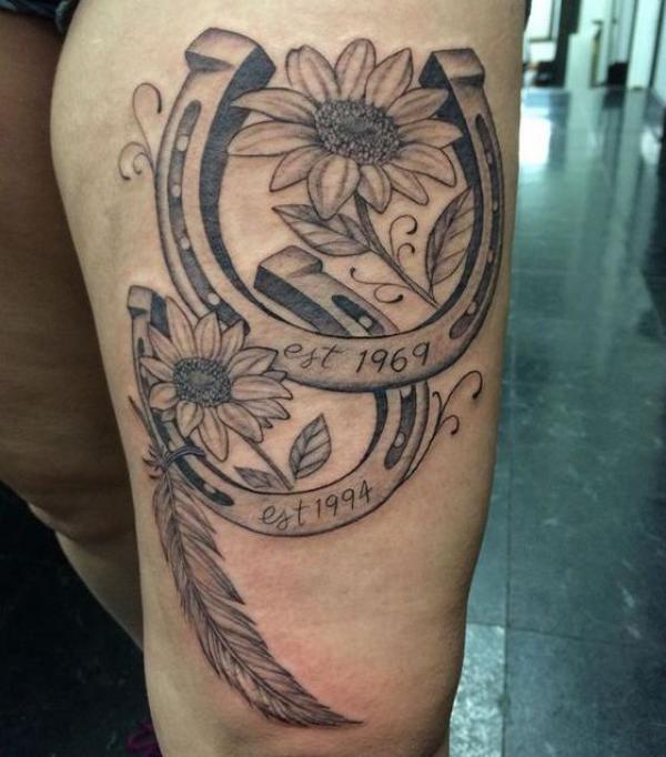 Black and grey horseshoe with feather and daisy tattoo