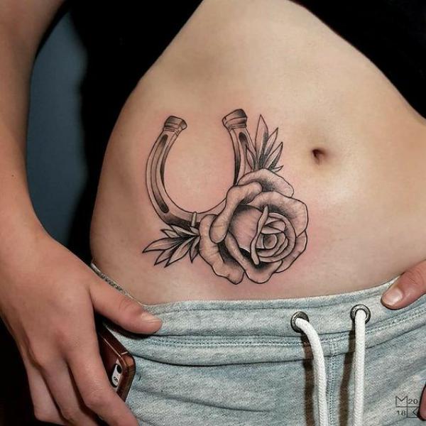 Black and white horseshoe with rose tattoo on the side of belly