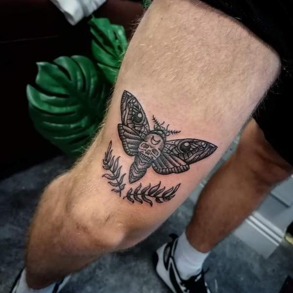 Death moth with fern tattoo above knee