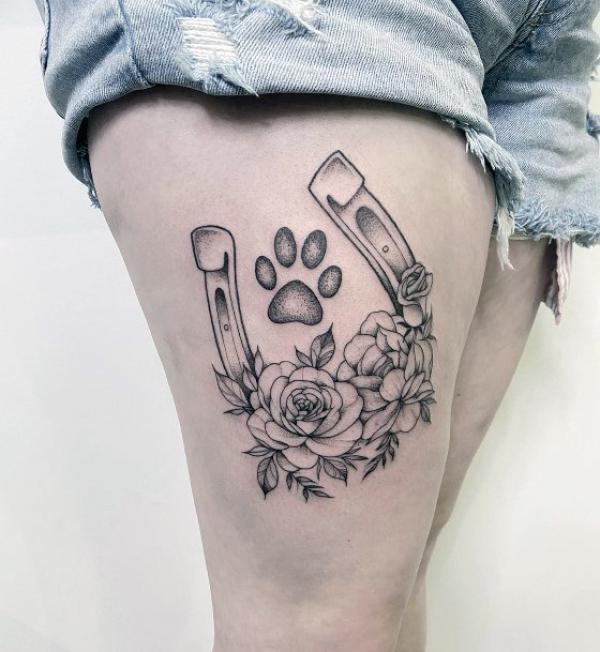 Feminine horseshoe with flower and paw print tattoo on thigh