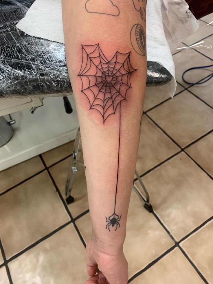 Heart spiderweb with a falling spider elbow tattoo