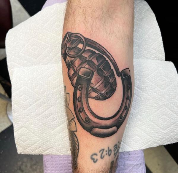 Horseshoe with a grenade tattoo on inner forearm