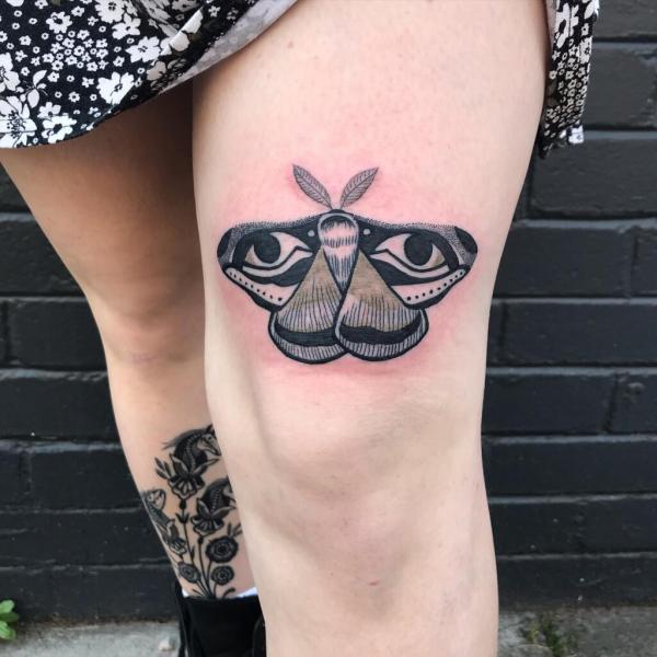 Moth with eyes above knee tattoo