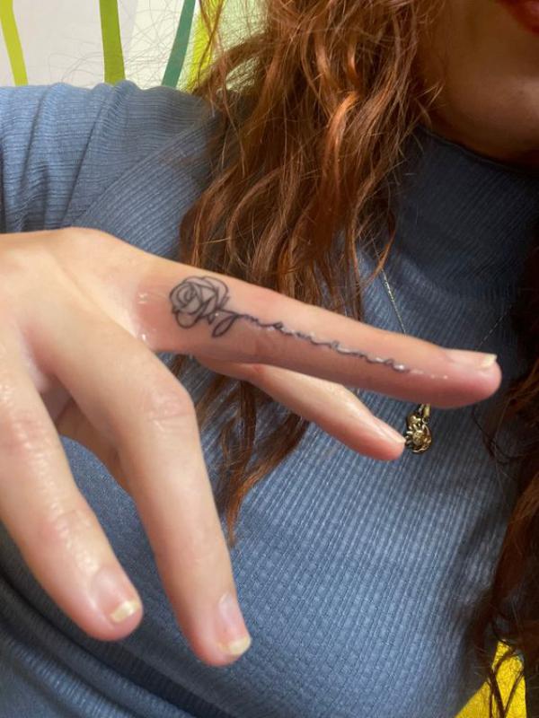 Rose outline with swirling stem tattoo on side of middle finger